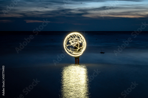 Figura luminosa en forma de planeta en playa al anochecer. Fotografía de larga exposición photo