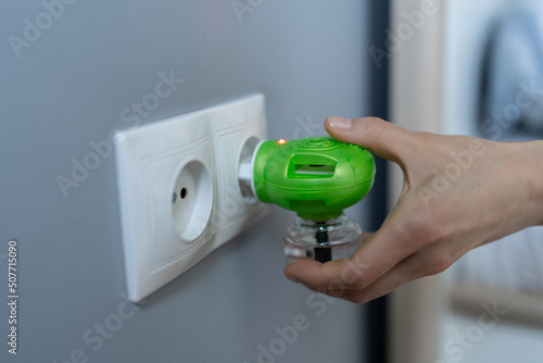 Fotografia Woman hand plugs mosquito repellent into the socket before going to bed
