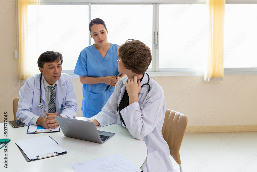 Multiracial medical team having a meeting with doctors in white lab coats and surgical scrubs seated at a table discussing a patients records, Medical team checking Xray results. Multiracial medical team having a meeting with doctors in white lab coats and surgical scrubs seated at a table discussing a patients records, Medical team checking Xray results.