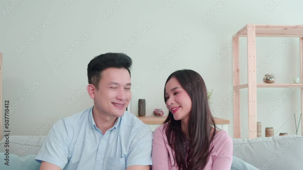 Happy sweet weekend time together lifestyle at home. Asian young attractive couple man and woman sitting on sofa in living room. Two person wife husband, while make eye contact with happy smile face. Happy sweet weekend time together lifestyle at home. Asian young attractive couple man and woman sitting on sofa in living room. Two person wife husband, while make eye contact with happy smile face.