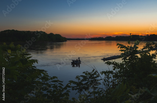 Several fishermen in a boat fishing in Midwestern River at sunset in late summer  beautiful colors reflect in calm water