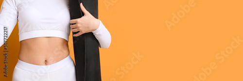 Sporty female coach holding yoga mat on orange background with space for text