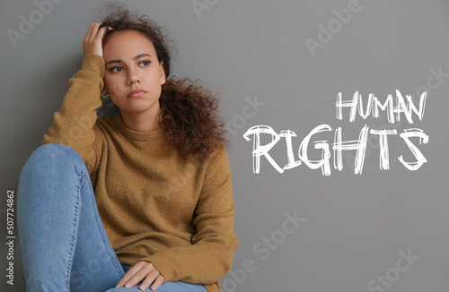 Fotografie Sad African-American woman sitting near grey wall. Human rights