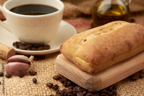 Rustic bread placed on a cutting board, around it a cup of American-style coffee, olive oil, coffee beans and garlic, placed in a vegetable fiber sack