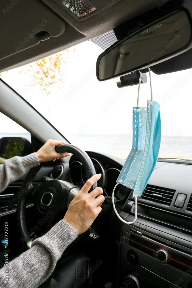 Medical mask hanging on rear view mirror in car of female driver