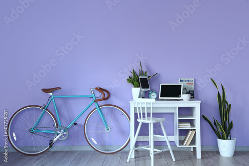 Comfortable workplace and bicycle near color wall in room interior