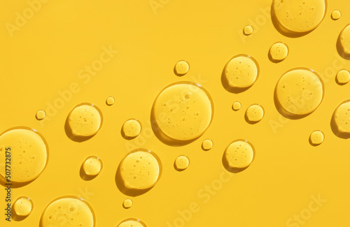 round drops of transparent gel serum on a yellow background