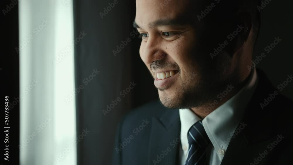 Confident businessman in classic blue suit tying or adjust necktie near window in hotel room at the morning. Handsome man wearing a nice suit on wedding day. Confident businessman in classic blue suit tying or adjust necktie near window in hotel room at the morning. Handsome man wearing a nice suit on wedding day.