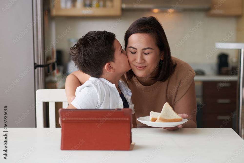 Adorable little boy kissing mother on cheeks after she brought him sandwiches for breakfast Adorable little boy kissing mother on cheeks after she brought him sandwiches for breakfast