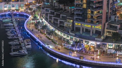 Waterfront promenade with palms in Dubai Marina aerial night timelapse.