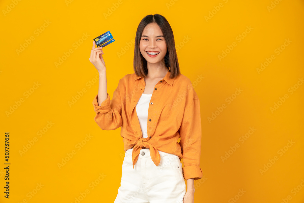 Cheerful beautiful Asian woman holding mockup credit card on yellow background. Cheerful beautiful Asian woman holding mockup credit card on yellow background.