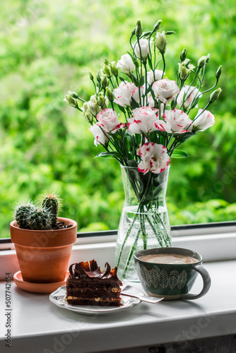 Cozy still life - a piece of chocolate cake, coffee, a bouquet of flowers on the window against the background of the garden