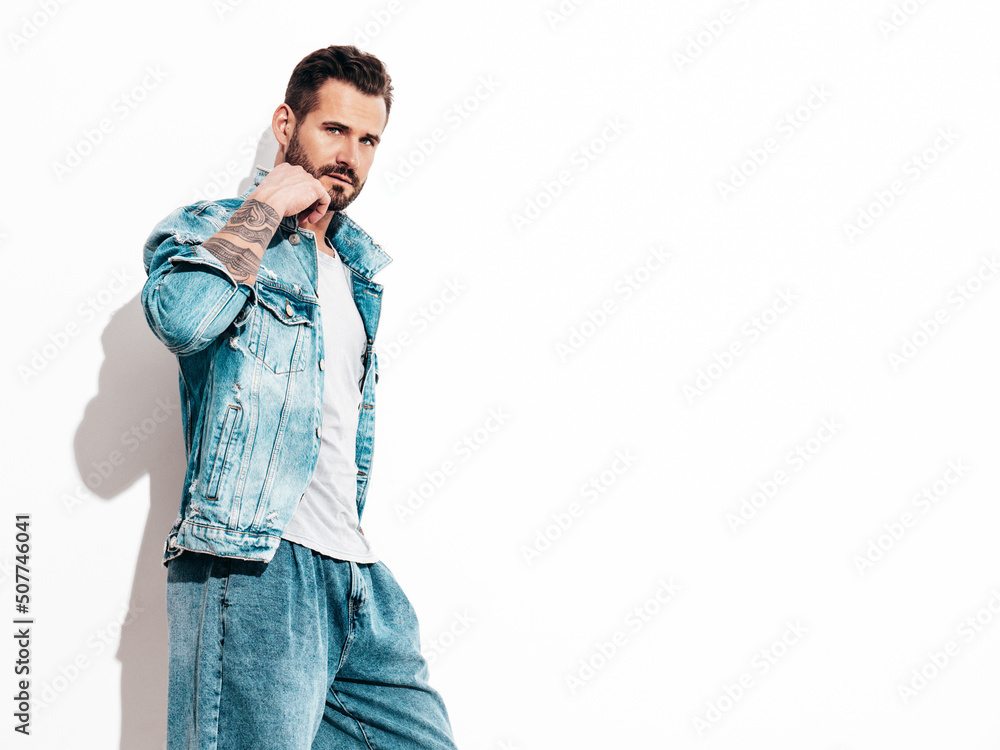 Portrait of handsome confident stylish hipster lambersexual model. Sexy man dressed in jeans jacket. Fashion male isolated on white wall in studio Portrait of handsome confident stylish hipster lambersexual model. Sexy man dressed in jeans jacket. Fashion male isolated on white wall in studio