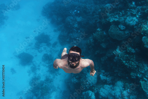 Underwater man swimming in blue crystal water looking at the camera