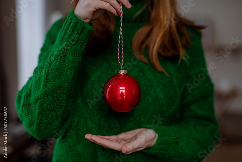 Woman wearing green sweater holding red Christmas ornament at home photo