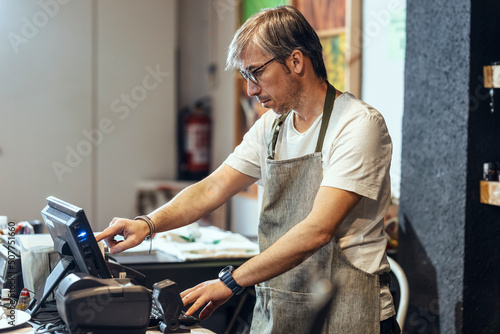 Store owner wearing eyeglasses using cash register at checkout in organic market photo