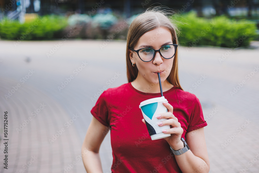 Happy young female with backpack smiling and looking away while walking on city street and enjoying fresh coffee to go Happy young female with backpack smiling and looking away while walking on city street and enjoying fresh coffee to go