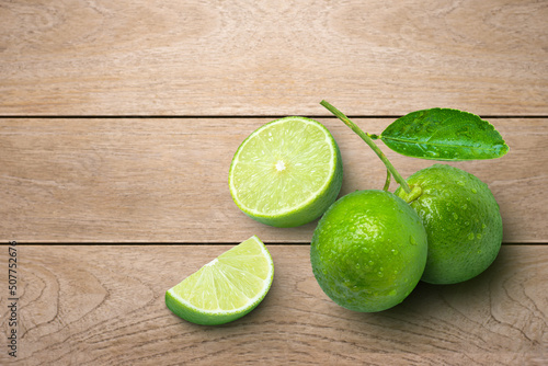 Lime fruits with green leaf and cut in half slice isolated on wooden table background. Top view. Flat lay. Copy space.