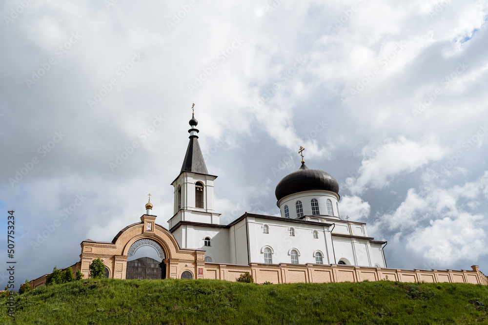 The White Church, the monastery gates, the brick wall, the bell tower, the Orthodox church stands on the mountain against the background of the sky.