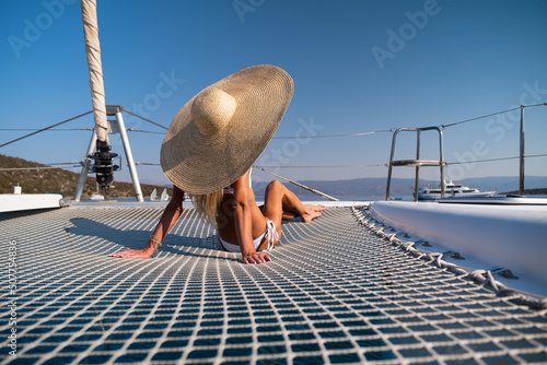 Fototapete Beautiful young blond woman in bikini sitting on catamaran bow at sunny summer d