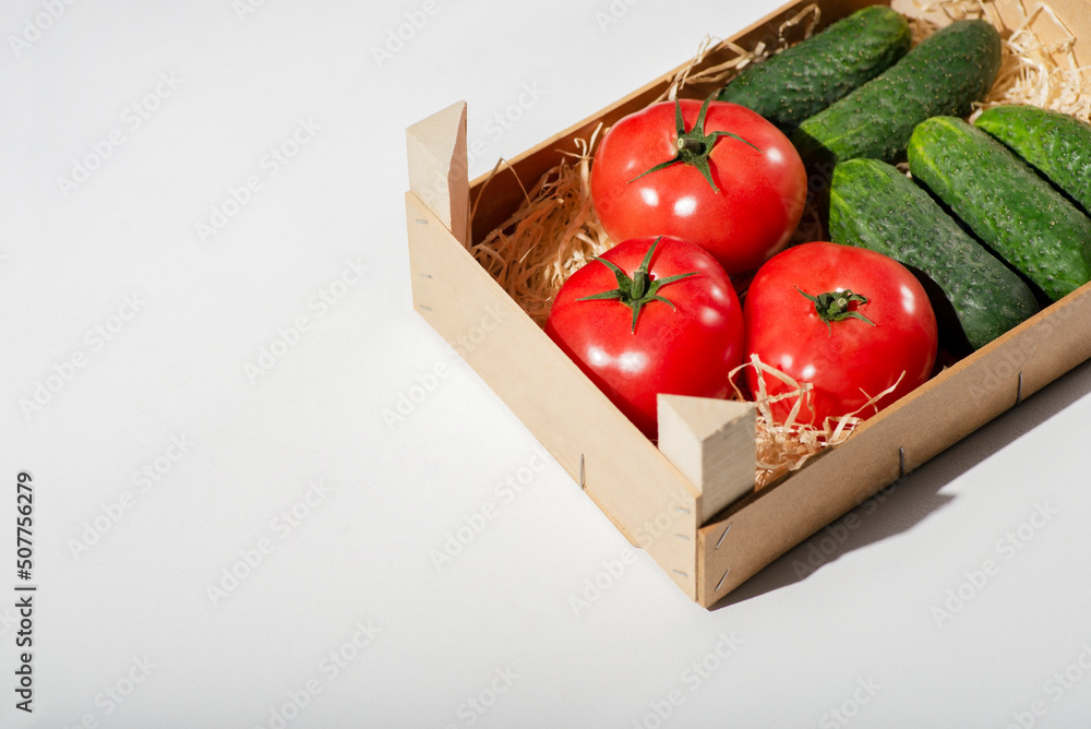 Tomatoes and cucumbers in a wooden box on white background. Farm organic vegetables, fresh harvest and nutrition concept. Place for text. Healthy eating Tomatoes and cucumbers in a wooden box on white background. Farm organic vegetables, fresh harvest and nutrition concept. Place for text. Healthy eating