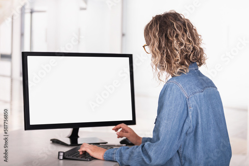 Rear side view of an unrecognizable woman in office using computer with blank screen to copy space
