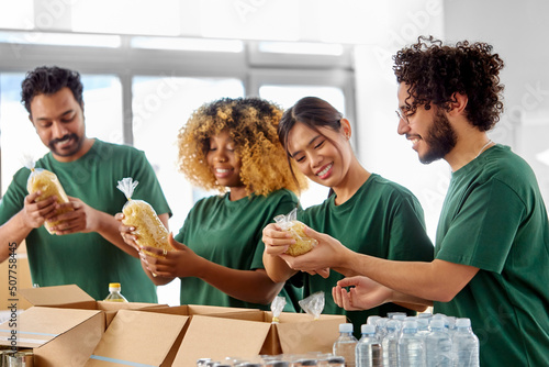 charity, donation and volunteering concept - international group of happy smiling volunteers packing food in boxes at distribution or refugee assistance center