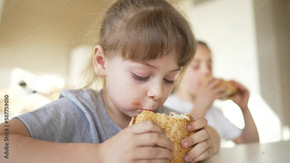 Family is eating sandwiches in school cafeteria. Students have lunch in cafeteria. Fast food between lessons. Nutrition in educational institutions. Children at the table eat burgers.fast food concept Family is eating sandwiches in school cafeteria. Students have lunch in cafeteria. Fast food between lessons. Nutrition in educational institutions. Children at the table eat burgers.fast food concept