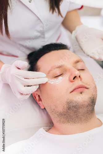 Cosmetologist applying anesthetic cream on man face in beauty salon