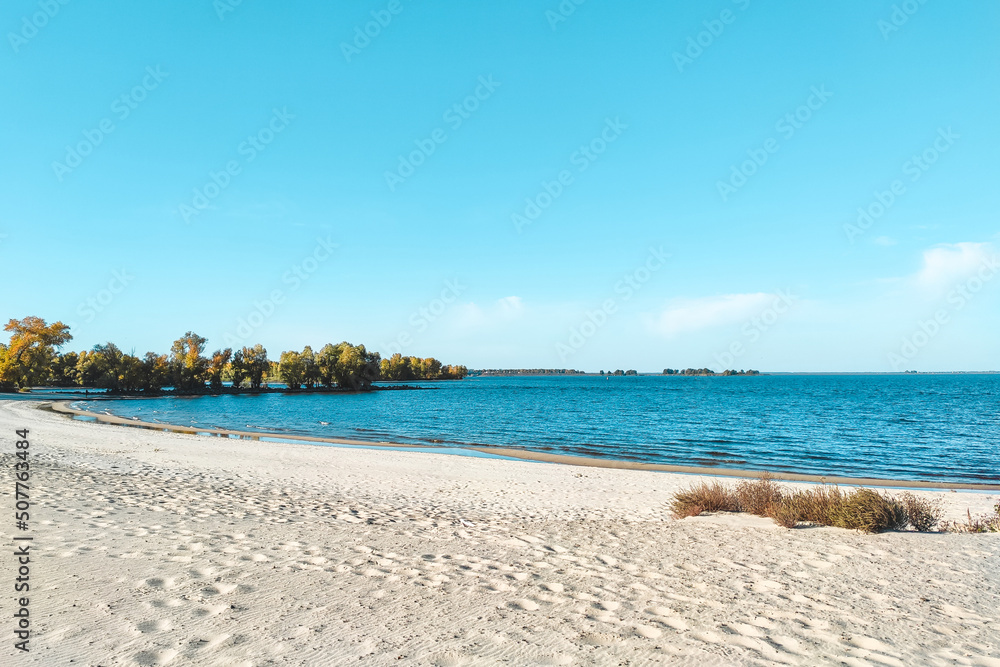 River beach landscape with blue water and green trees.