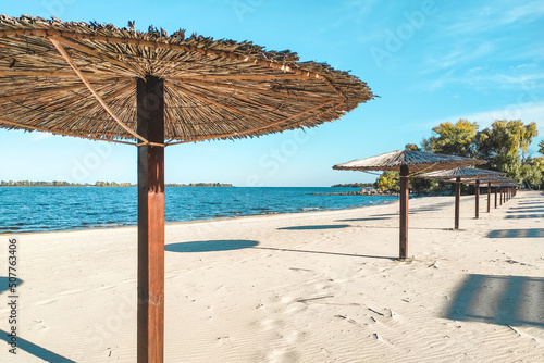 Straw beach umbrellas for shade near the river on the background of the landscape.