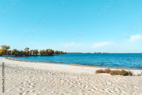 River beach landscape with blue water and green trees.