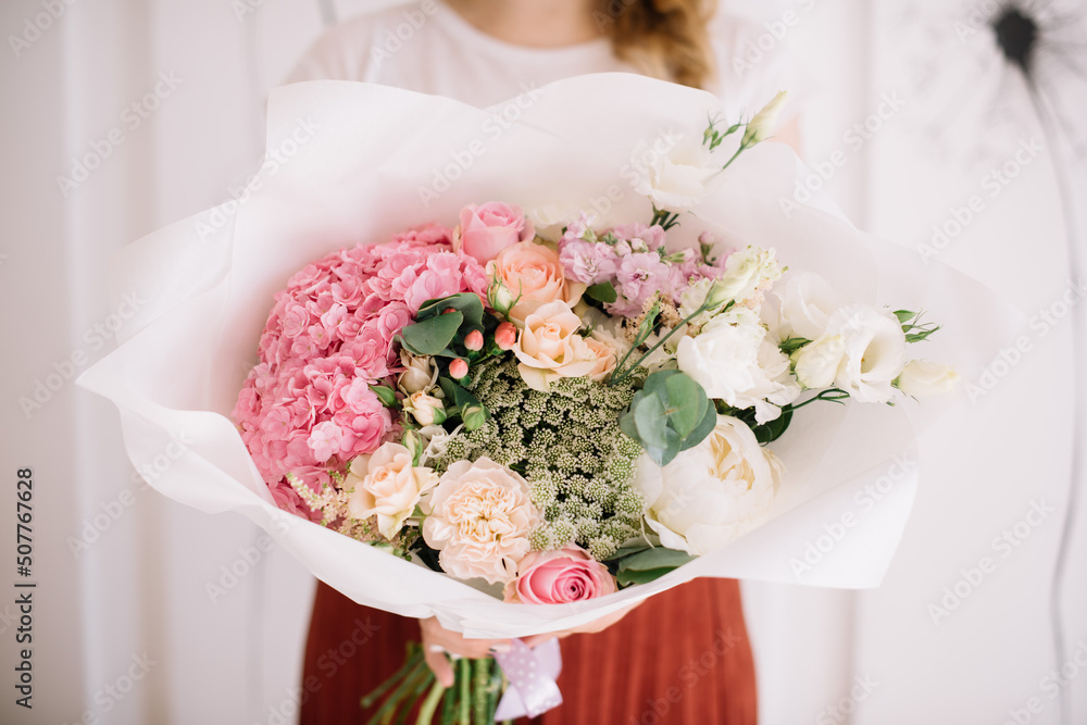 Very nice young woman holding big and beautiful flower bouquet of fresh hydrangea, roses, ammy, carnations, eustoma, peony in white and pink colors Very nice young woman holding big and beautiful flower bouquet of fresh hydrangea, roses, ammy, carnations, eustoma, peony in white and pink colors