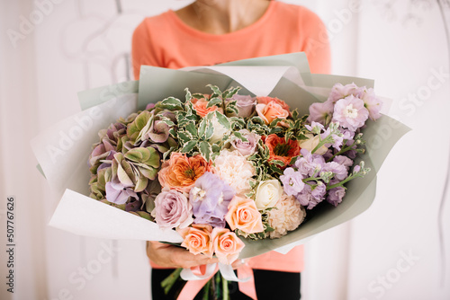 Very nice young woman holding big and beautiful bouquet of fresh hydrangea, roses, matthiola, carnations in pastel peach and purple colors, cropped photo, bouquet close up