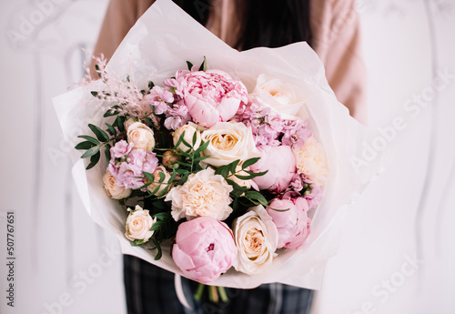 Fototapeta Naklejka Na Ścianę i Meble -  Very nice young woman holding big and beautiful bouquet of fresh peonies, roses, pistachio, carnations, matthiola in pink and cream colors, cropped photo, bouquet close up