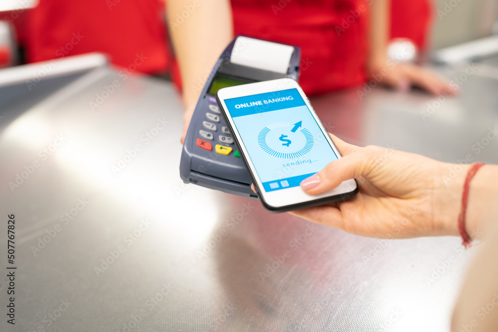 High angle close-up shot of unrecognizable young woman using online banking technology on smartphone to pay for goods in store