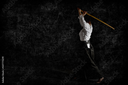 A girl in black hakama standing in fighting pose with wooden sword bokken over black background. Shallow depth of field. Grunge. photo
