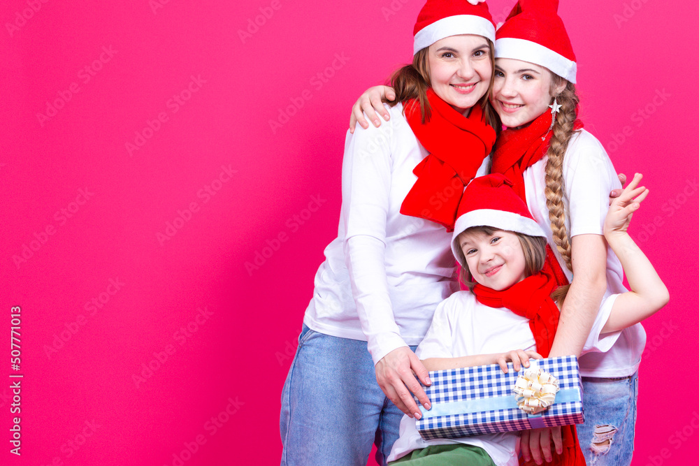 Fototapeta premium Holidays Ideas and Concepts. Three Happy Caucasian Girls Wearing Santa Hats Having Fun Together While Cuddling To Each Other With New Year Gifts and Present Boxes Over Pink.