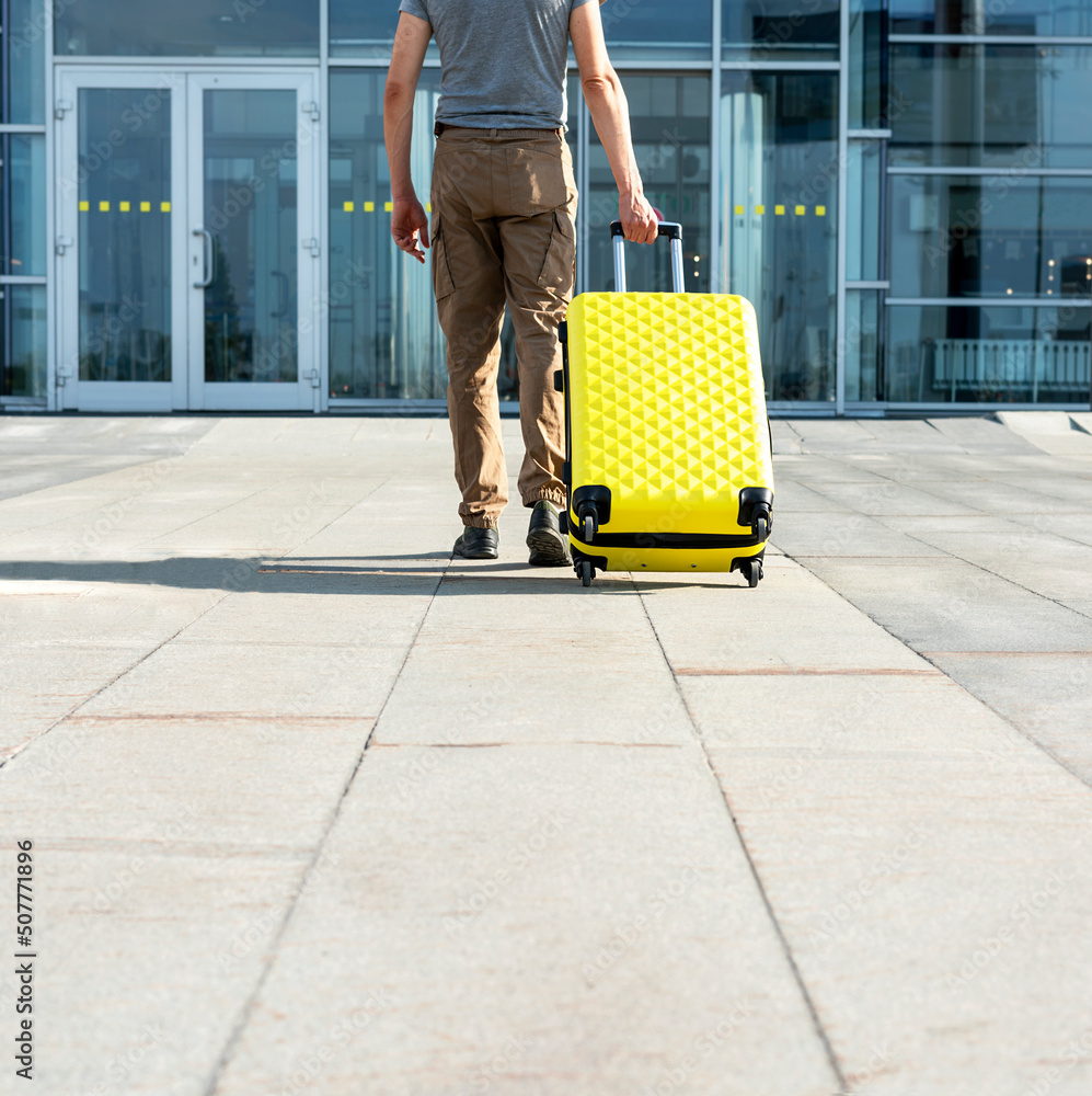 rear view of young man traveler in casual clothes carrying a yellow suitcase next to the entrance to the airport outside tourism concept of air flights travel and vacation rear view of young man traveler in casual clothes carrying a yellow suitcase next to the entrance to the airport outside tourism concept of air flights travel and vacation