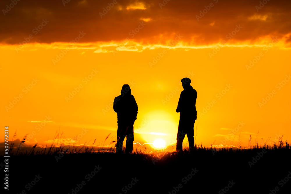 Two silhouettes of men talking at sunset or sunrise with dramatic sky and clouds.Dialogue and meeting two people on the horizon and skyline.Outlines of people in the sunlight.Golden hour with friends Two silhouettes of men talking at sunset or sunrise with dramatic sky and clouds.Dialogue and meeting two people on the horizon and skyline.Outlines of people in the sunlight.Golden hour with friends
