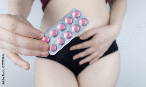 Tablets for pain during menstruation. Pain during menses. The concept of critical days for a woman. The girl stands on a white background and holds medicines for pain in her hands. Painkillers