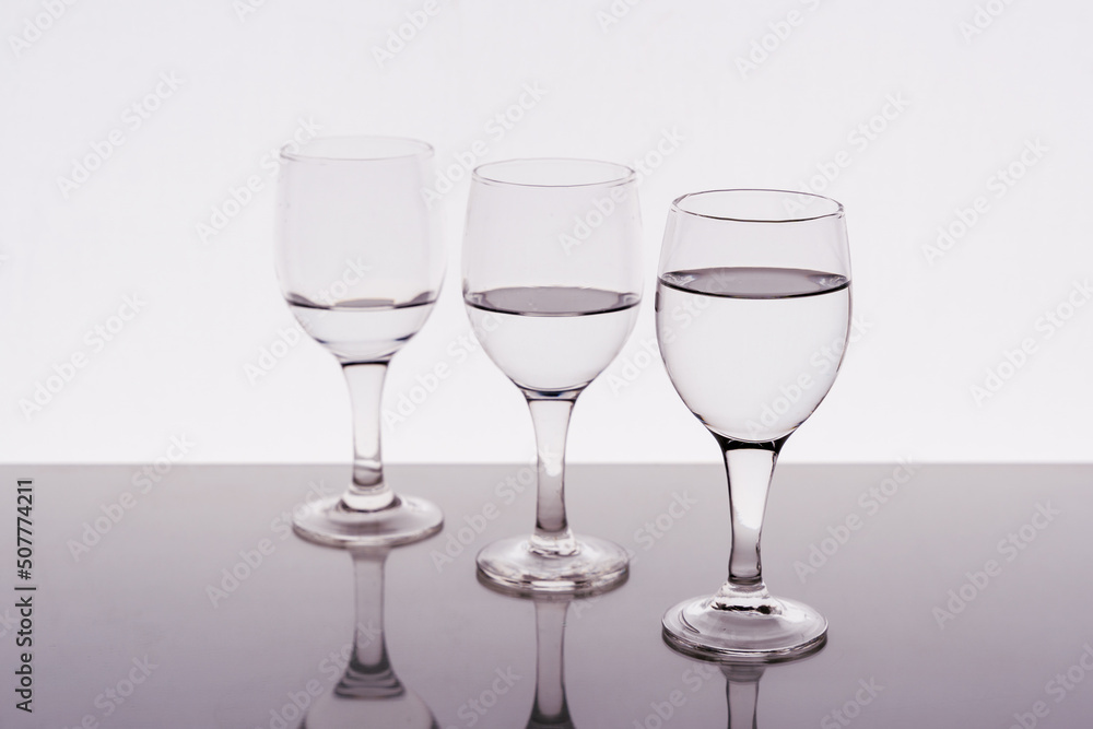Three wine glasses filled with water reflected on the table Three wine glasses filled with water reflected on the table