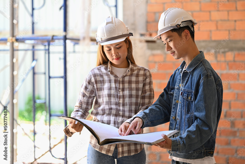 Young engineers supervising progress of construction project together. Industry, Engineer, construction concept Young engineers supervising progress of construction project together. Industry, Engineer, construction concept