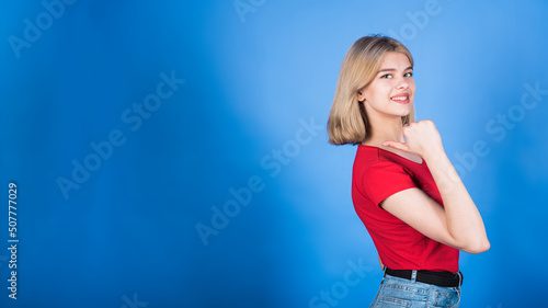 Young and attractive blonde caucasian girl in casual clothes pointing her thumb at copy space for advertising isolated on blue studio background. © Павел Костенко