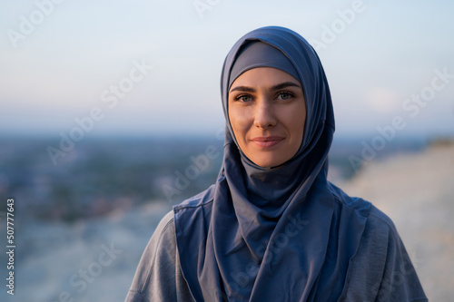 Portrait of a young beautiful girl in a hijab looking at the camera on a background of sunset and landscape