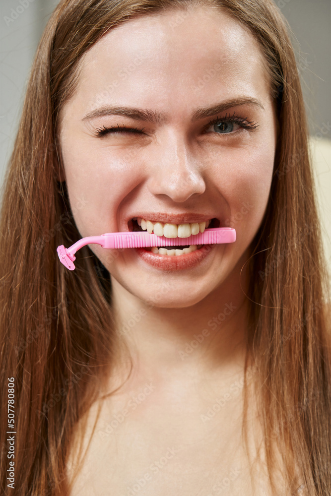 funny young woman holding a pink razor in her teeth. unwanted hair removal funny young woman holding a pink razor in her teeth. unwanted hair removal