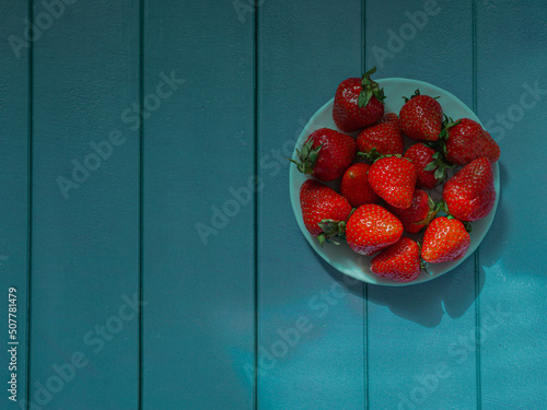 Strawberries on a white saucer on a wooden background from wooden planks