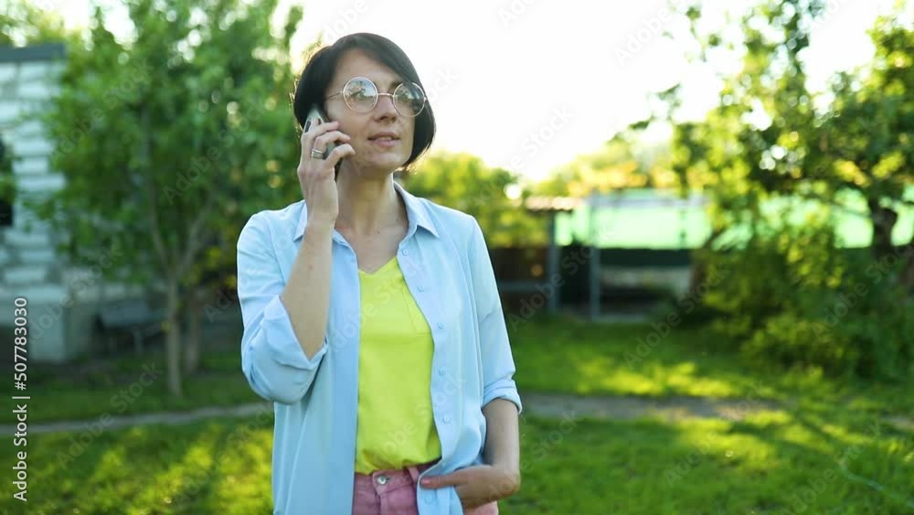 Happy woman in glasses talking on mobile phone outdoor, concept of leisure time with gadgets outdoors at home. Happy woman in glasses talking on mobile phone outdoor, concept of leisure time with gadgets outdoors at home.