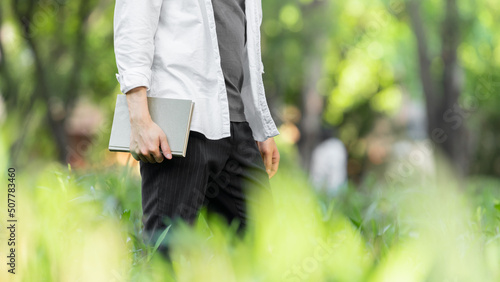 Fotografie Asian young man holding a book is walking in the park