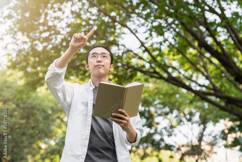 Asian young man is reading a book   outdoors at the park 